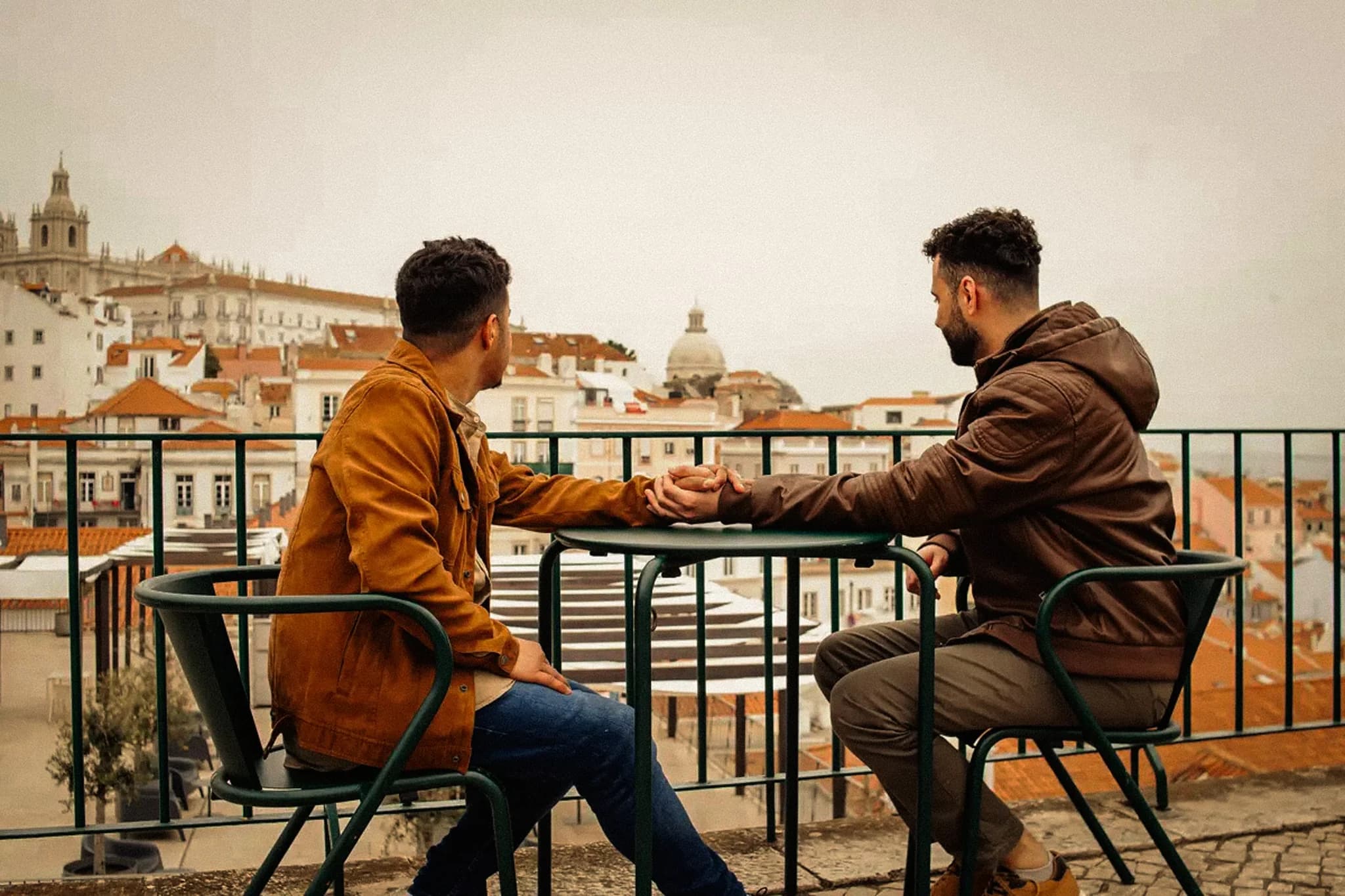 Two men holding hands on a rooftop overlooking the city